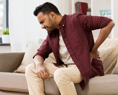 Man on sofa gripping lower back in pain