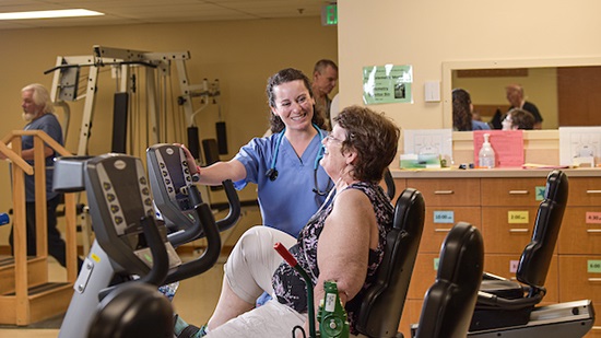 woman on exercise bike with nurse assisting
