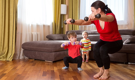 Woman exercising at home with two small children next to her