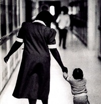 old black and white photo from behind a nurse walking holding the hand of a toddler