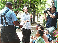 Photo of a cameraman recording a man speaking to kids