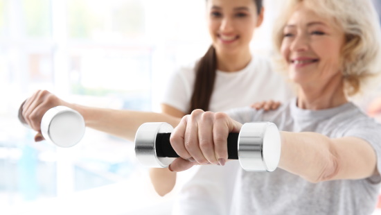 Senior woman lifting hand weights with therapist