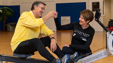 Dr. Michael Fisher sits on a rowing machine while talking with Barbara Jarrell, a YMCA LiveSTRONG instructor.