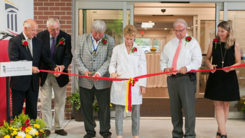 Six people stand behind a red ribbon, holding scissors and are preparing to cut the ribbon.