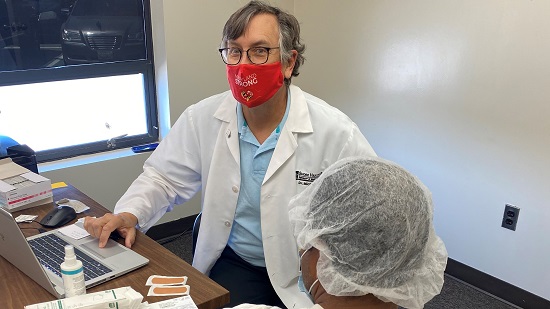 Dr. Michael Fisher looks at the camera as a patient waits to receive the COVID-19 vaccination.