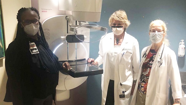 Three members of the Clark Comprehensive Breast Center team stand around a mammography machine.