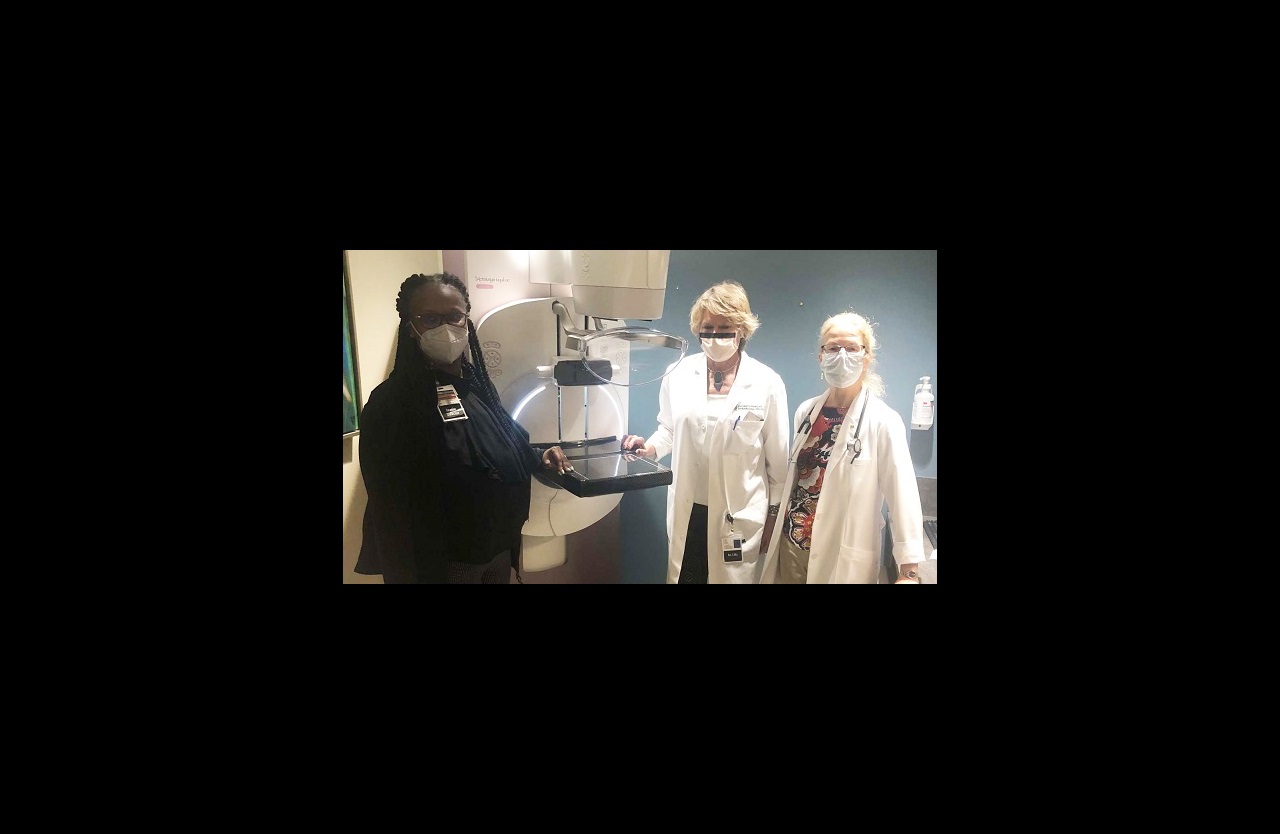 Three members of the Clark Comprehensive Breast Center team stand around a mammography machine.
