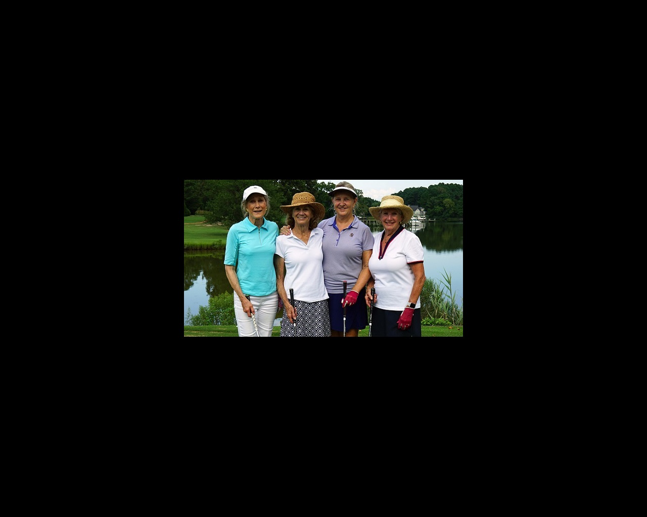 Four women stand side by side with their golf clubs on a golf course.