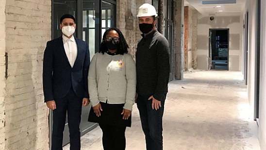 Three people stand in front of a long hallway in a building under construction.