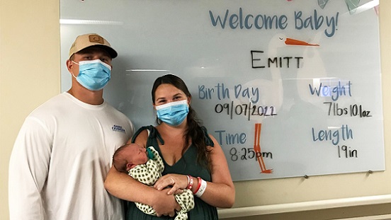 A woman holds a newborn baby, standing next to her husband, in front of the Welcome Baby board at UM Shore Medical Center at Easton's Birthing Center. The sign is customizable with the baby's birth statistics and name.