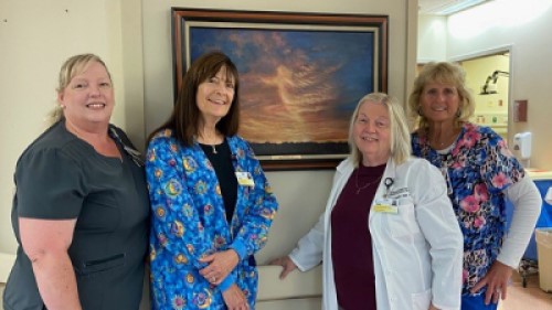 Team members from the Pain Management Center at UM Shore Regional Health stand in front of a painting of a sunset.