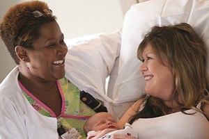 Photo of a caregiver smiling with a mother holding a new baby