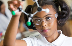Young girl wearing safety glasses looking at a molecular structure model