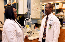 Two physicians wearing lab coats standing in the lab talking