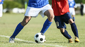 A close-up photo of two soccer players from the torso down, competing for possession of the ball.