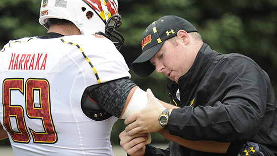 Athletic trainer Mike Smuda bandages up a football player's elbow.