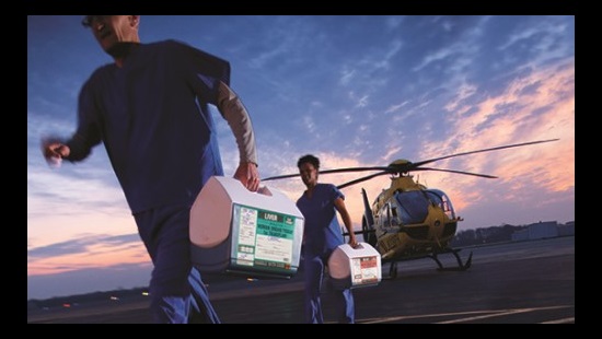 Two people getting of a helicopter carrying coolers that hold organs to be transplanted