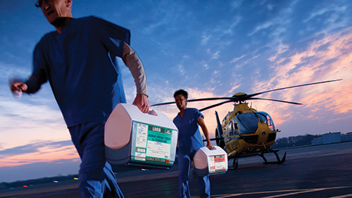 Two healthcare professionals walking away from a helicopter with coolers carrying organs
