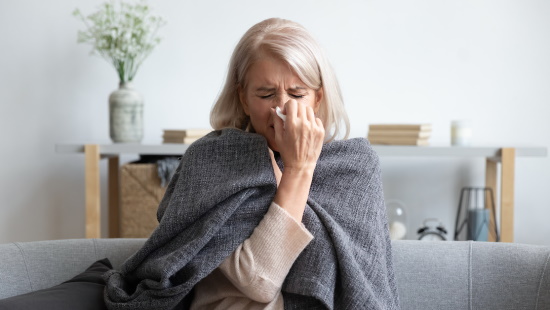 Woman wrapped in blanket with tissue on her nose