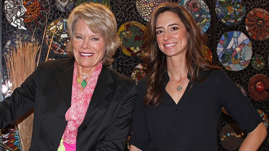 Two women stand in front of a mosaic smiling. 
